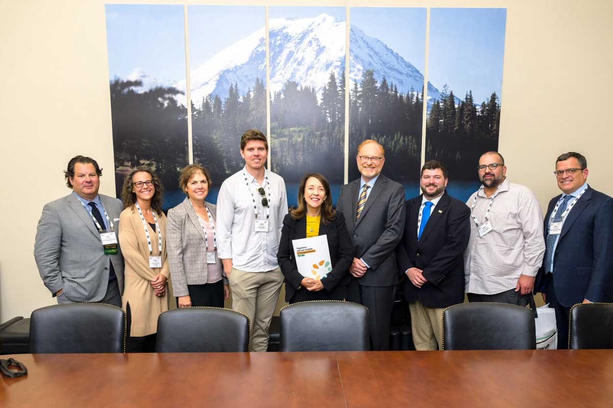 A group of nine Washington Conference attendees pose for a picture in a conference room. Behind the group is a picture of a mountain.