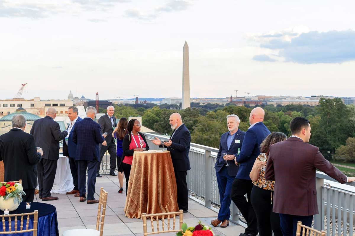 A group of Washington Conference attendees enjoy cocktails with the Washington Monument in the background.