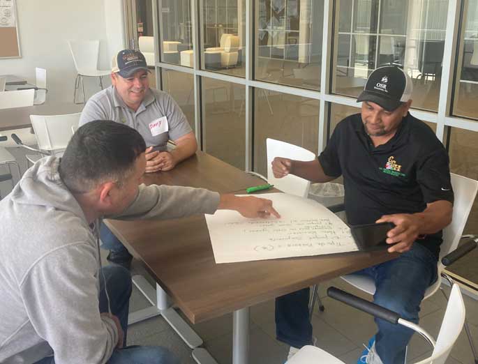 Three gentlemen sit at a table and complete training at Windset farms.